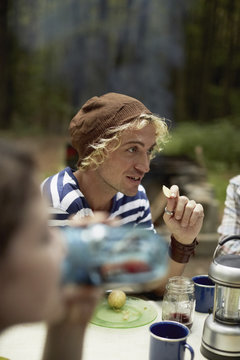 A young man sitting at a picnic table in the woods.