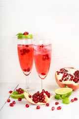 Two glasses with red pomgranate champagne, lime and mint.