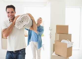 Smiling couple carrying rolled rug after moving in house