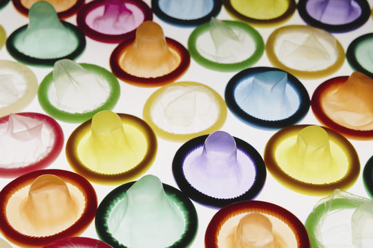 A large group of multi-colored condoms displayed on a white background. Laid out neatly.