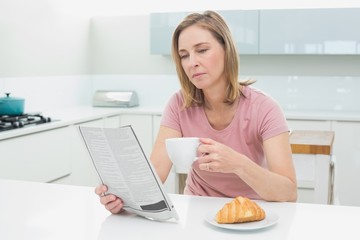 Concentrated woman reading newspaper while having coffee in