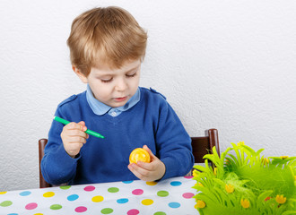 Little toddler boy painting traditional Easter egg for hunt