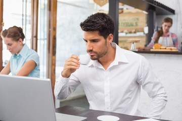 Man drinking coffee while using laptop in coffee shop