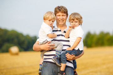 Young father and two little twins boys having fun on yellow hay