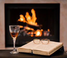 glass of cognac and book by the fireplace