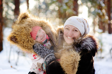 mother and little girl laughing in winter forest