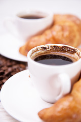Two ceramic cups of black coffee and croissants