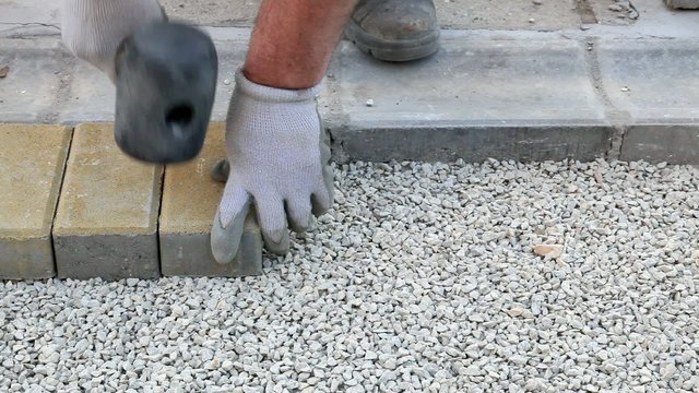 Worker installing brick paver, using hammer