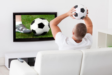 Soccer fan watching a game on television holding a soccer ball