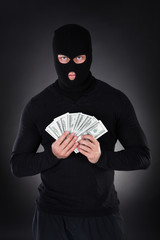 Criminal in a balaclava holding a fistful of money