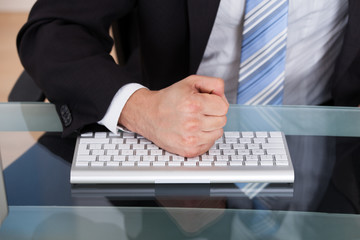 Midsection of businessman pounding fist on keyboard