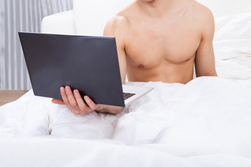 Midsection Of Shirtless Man Holding Laptop In Bed