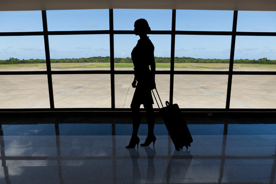 Businesswoman with baggage walking against airport window