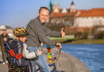 Father with son riding by bicycle along the river waterfront in