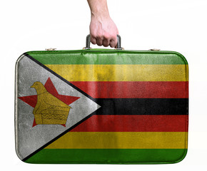 Tourist hand holding vintage leather travel bag with flag of Zim