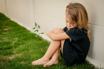 Portrait of sad little girl sitting near  wall in the day time
