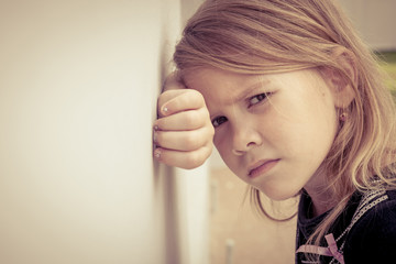 Portrait of sad little girl sitting near  wall in the day time