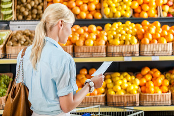 Girl looks through shopping list near the pile of fruits