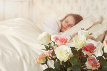 Beautiful sleeping woman in bed with roses