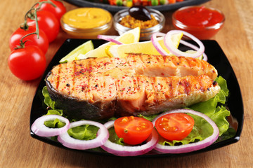 Tasty grilled salmon with lemon and vegetables, on wooden table