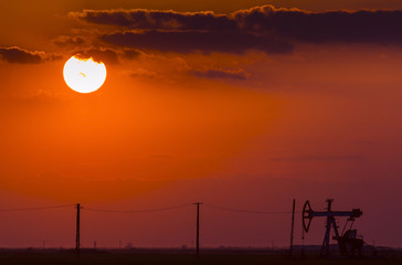 Oil and gas well profiled on sunset sky