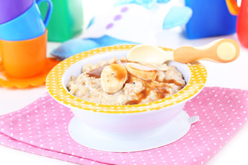 Bowl of porridge for baby on toys background