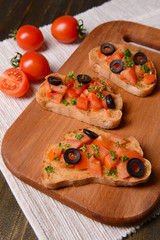 Delicious bruschetta with tomatoes on cutting board close-up