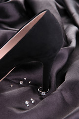 Beautiful ring on heel of black female shoe, on silk background