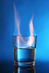 Glass with burning alcohol on blue background