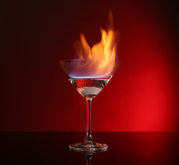 Glass with burning alcohol on red background