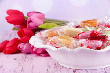 Tasty candies in bowl with flowers on table on bright