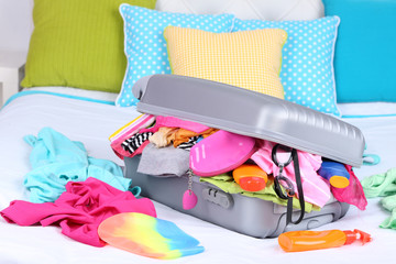 Grey suitcase with clothing on bed close-up