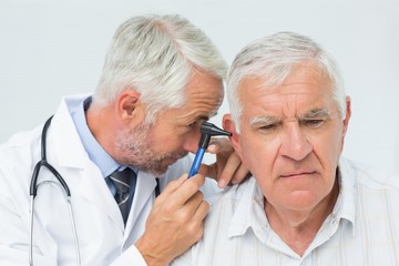 Male doctor examining senior patient's ear