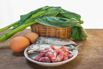 Fish, pork, eggs and kale on a wooden floor.
