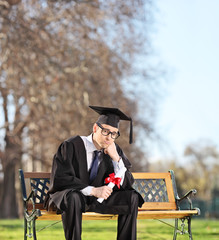 Sad graduate student sitting on a bench in park