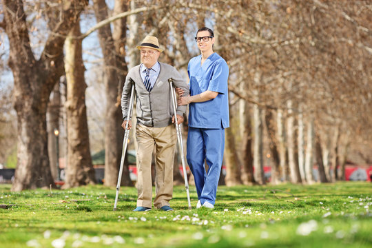 Senior and a male nurse walking in park