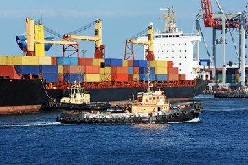 Tugboat assisting container cargo ship to harbor quayside