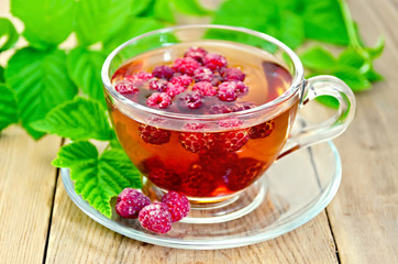 Tea with raspberry and green leaves on board