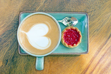 Cup of coffee, heart shape with strawberry biscuit on wood