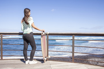 beautiful young skater woman with a longboard near the sea