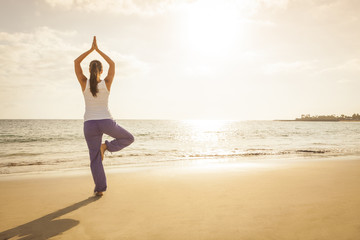 Young woman practicing tree yoga pose near the ocean during suns