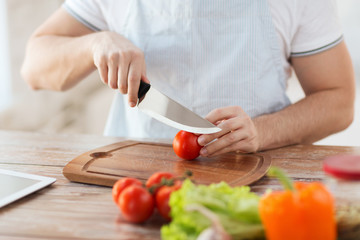 male hand cutting tomato on board with knife