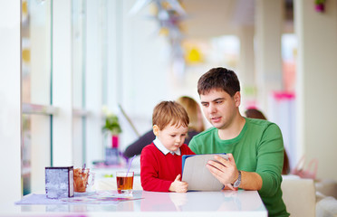 father and son with tablet in colorful cafe