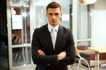 Confident businessman standing with arms folded at office