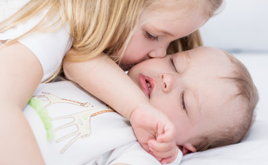 little girl kisses a sleeping baby brother