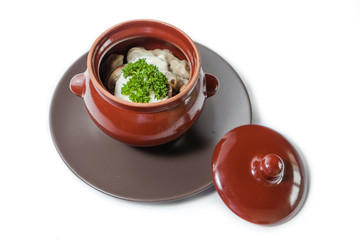 Pelmeni with sour cream and mushrooms in a clay pot