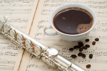 Silver flute,cup of coffee on an ancient music score background