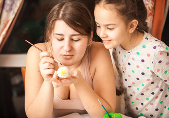 Closeup portrait of mother showing daughter how to paint eggs