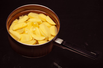 Raw peeled potatoes in pot pan on black. Healthy food.