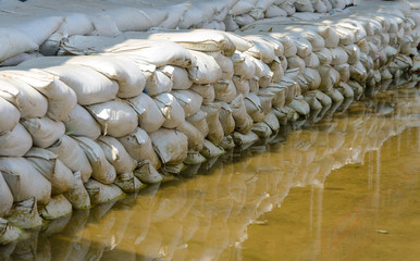 White sandbags for flood defense and it's reflection brown water